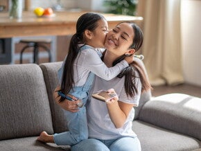 Preschool-age child kisses her mom, a solo parent, while they’re in the living room.