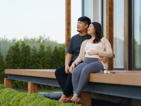 Asian pregnant couple sit on the porch of their vacation home during their babymoon