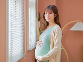 Asian woman, who is 39 weeks pregnant, holds her belly bump and smiles at the camera.