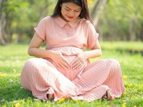 Folic Acid: A Pre-Pregnancy Must-have Asian pregnant woman sitting on grass touches her belly, forming a heart shape with her fingers.