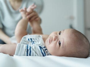 A young Asian mother changing her baby's diaper on a bed.