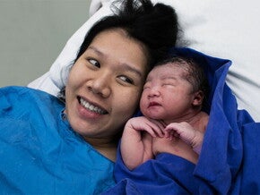 Smiling Asian mom glances at her newborn after skin-to-skin contact in the delivery room