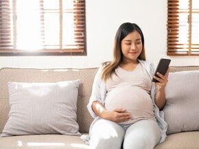 Smiling Asian pregnant woman who is 38 weeks pregnant checks her phone Smiling Asian pregnant woman who is 38 weeks pregnant checks her phone