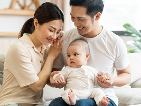 Smiling mother and father holding newborn son at home, considering birth control methods for family planning