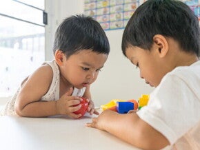 Asian toddler intently stares at the toy of another child.