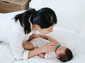 Asian mom giving pacifier to little Asian newborn.
