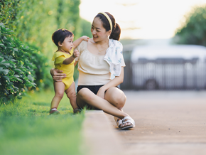 Young Asian mom supports her baby who's practicing their motor skills while outdoors. Young Asian mom supports her baby who's practicing their motor skills while outdoors.