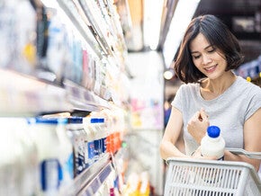 Young Asian woman putting a milk bottle in her basket after choosing from the types of milk in the supermarket