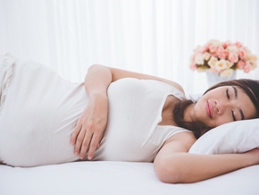 Young pregnant Asian woman lies on her left side in bed, one of the ideal pregnancy sleeping positions