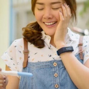 Asian woman in denim jumping smiling at pregnancy test results. Asian woman in denim jumping smiling at pregnancy test results.