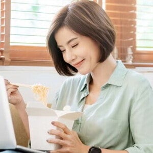 Young Filipina experiences a food craving and enjoys takeout while sitting on the sofa with her laptop on her lap. Young Filipina experiences a food craving and enjoys takeout while sitting on the sofa with her laptop on her lap.