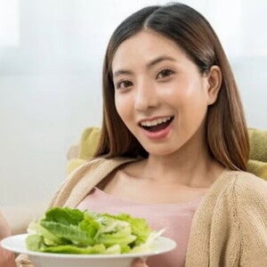 Asian pregnant woman eating greens on sofa. Asian pregnant woman eating greens on sofa.