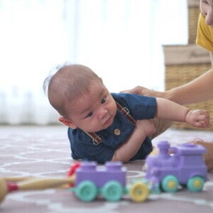 A young Asian woman playing with a baby boy on the floor using educational toys.