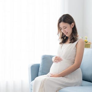 A 29 weeks pregnant Asian woman lovingly holding and looking at her belly at home