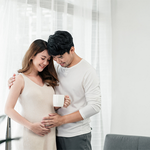A 7 weeks pregnant Asian woman standing while her husband holds her close with a hand on her belly A 7 weeks pregnant Asian woman standing while her husband holds her close with a hand on her belly