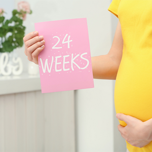 A cropped photo of 24 weeks pregnant Asian woman holding a card with the text 24 WEEKS near her belly