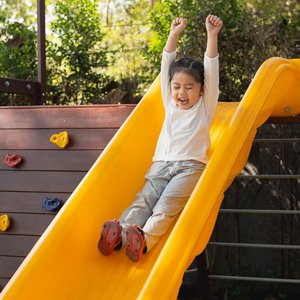 A happy child sliding down a playground slide outdoors, representing active play, childhood joy,  and the importance of supporting kids’ immune and respiratory health