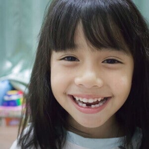 A little Asian girl smiling widely to show her teeth, which have a gap at the bottom.