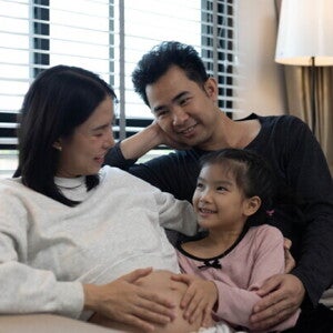 A pregnant woman and her husband with their stepdaughter on a couch, happy as a blended family.