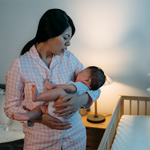 A sleepy Asian mom in pajamas carrying her newborn, who’s fussy because of colic in babies A sleepy Asian mom in pajamas carrying her newborn, who’s fussy because of colic in babies