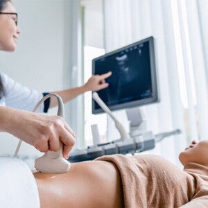 A smiling Asian pregnant woman undergoes an ultrasound scan with her ob-gyn for pregnancy complications A smiling Asian pregnant woman undergoes an ultrasound scan with her ob-gyn for pregnancy complications