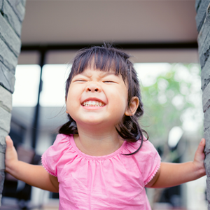 A smiling Asian toddler between two stone pillars with smiling to show her healthy milk teeth.