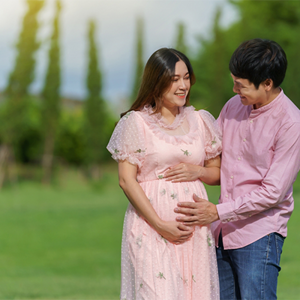 A woman who is 15 weeks pregnant cradles her baby bump as she and her husband walk in the park.