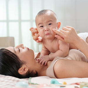 A young Asian mom lying in bed keeping her tearful baby close to her, knowing why babies cry