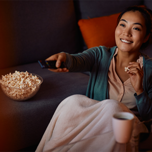 A young Asian mom relaxing on the sofa with a bowl of snacks, watching mom movies
