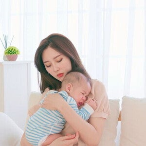 A young Asian mother carrying and soothing her baby on the sofa, worrying about colds in newborns.