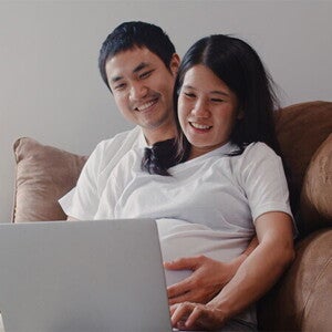 A young Asian pregnant couple with a laptop at home, applying online for the expanded maternity leave A young Asian pregnant couple with a laptop at home, applying online for the expanded maternity leave