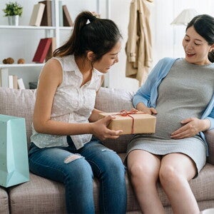 A young Asian pregnant woman receiving a gift from her friend during her baby shower at home. A young Asian pregnant woman receiving a gift from her friend during her baby shower at home.