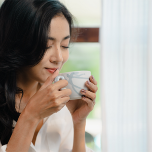 A young Asian woman enjoys a cup of coffee beside the window as part of her morning routine
