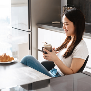 A young Asian woman is sitting in the kitchen drinking coffee during pregnancy