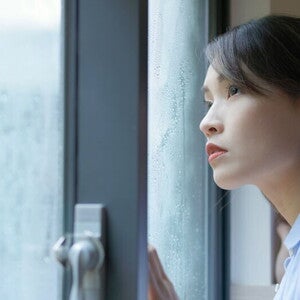 A young Asian woman, looking out at the rain, wondering what typhoon safety precautions to take for her family. A young Asian woman, looking out at the rain, wondering what typhoon safety precautions to take for her family.