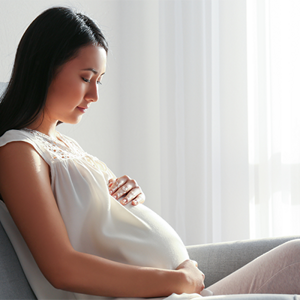 A young woman holding her belly while seated at 16 weeks pregnant.