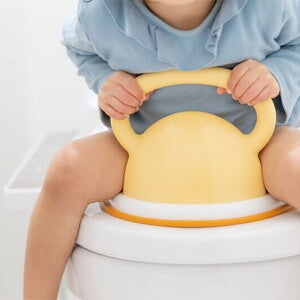 An Asian child sits on a toilet bowl with a potty training seat.