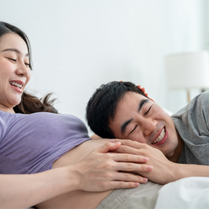 An Asian husband putting his ear to his 14 weeks pregnant wife’s belly in the bedroom. An Asian husband putting his ear to his 14 weeks pregnant wife’s belly in the bedroom.