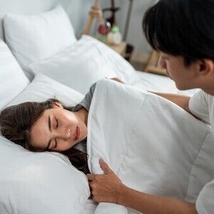 An Asian man puts a blanket on his wife with a headache and lets her rest, helping her through early pregnancy pain areas
