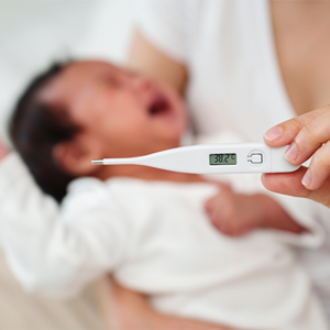 An Asian mom checks her her baby for fever using a thermometer
