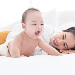 An Asian mother watching her smiling 6-month-old baby trying to crawl on the bed An Asian mother watching her smiling 6-month-old baby trying to crawl on the bed