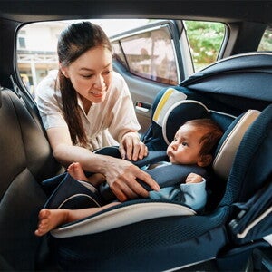 An Asian woman fastening her infant into a rear-facing car seat.