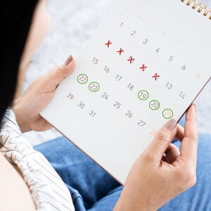An Asian woman holding a calendar marked to show her menstrual cycle and fertile window An Asian woman holding a calendar marked to show her menstrual cycle and fertile window