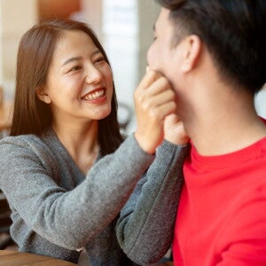 Young Asian woman pinches her partner's cheeks as they talk responsible parenthood. 
