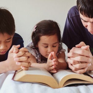 Asian dad with young son and little girl praying on the bed at home, one of their Filipino traditions.