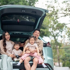 A happy Asian family sitting in the trunk of their car, enjoying a pit stop on their road trip.