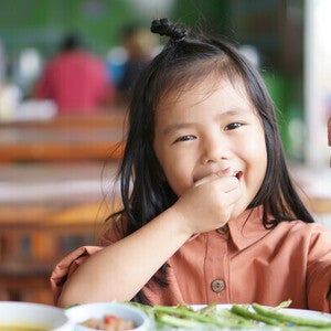 Preschooler picky eater Asian girl enjoying eating vegetables with her hands.