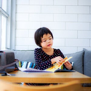 Asian little girl playing with a sticker book, one of her visual learning tools.