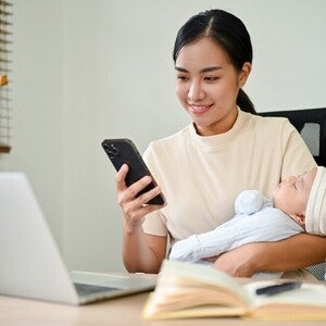 Filipino mom checks her PhilHealth contribution for self-employed members on her phone while holding her baby.