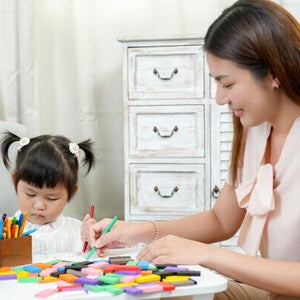 A young Asian mom teaching her little girl to color—one of the fun activities for kids at home to keep them busy.